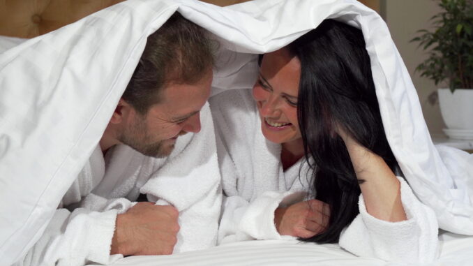 Happy mature couple laughing joyfully, lying in bed together.