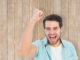 Happy casual man cheering at camera against wooden planks