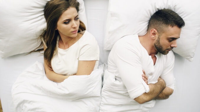 Top view of young upset couple lying in bed have problems after quarrel and angry to each other at home