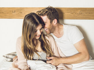 Couple of happy girl and guy smiling in their bed at home.