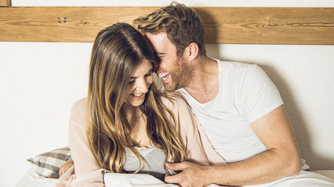 Couple of happy girl and guy smiling in their bed at home.