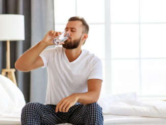Young healthy man drinking water in morning at window