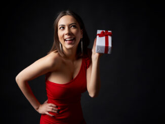 Happy playful woman in red evening gown holding a gift box