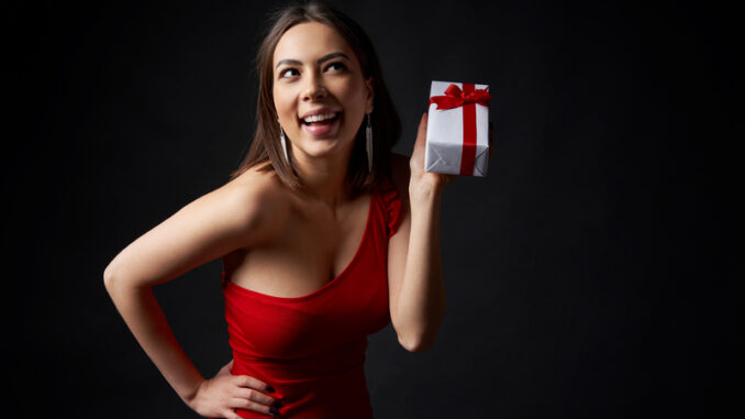 Happy playful woman in red evening gown holding a gift box