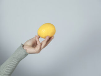 Woman hand holding lemon on gray wall background