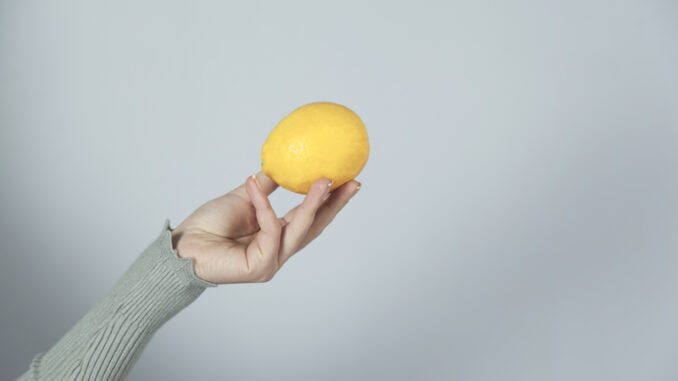 Woman hand holding lemon on gray wall background