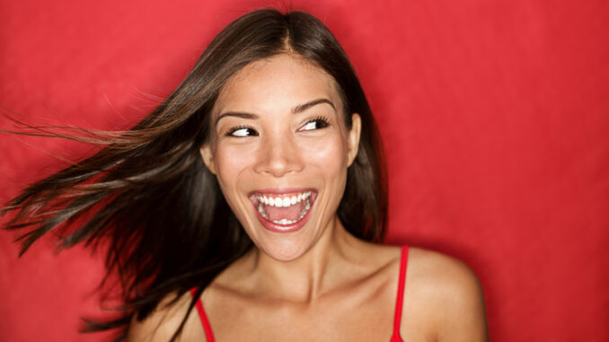 Happy excited woman looking to the side screaming cheerful with wind in the hair on red background.