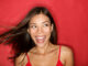 Happy excited woman looking to the side screaming cheerful with wind in the hair on red background.