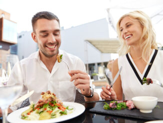 happy couple eating salad for dinner at cafe or restaurant terrace