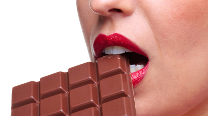 Close up of a woman with red lipstick eating a bar of chocolate