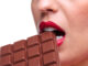 Close up of a woman with red lipstick eating a bar of chocolate