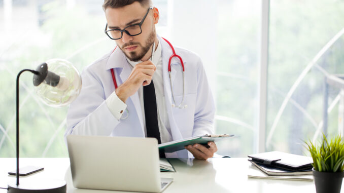 young Handsome man Doctor with stethoscope working with laptop computer and writes a medicine recipe in hospital