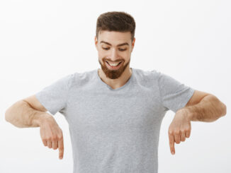 Portrait of happy and amazed good-looking masculine male with perfect hairstyle and beard looking and pointing down with delight and curiosity enjoying watching downwards at interesting copy space.