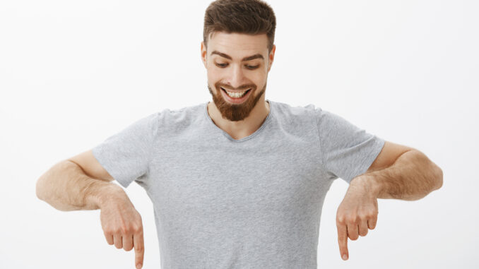 Portrait of happy and amazed good-looking masculine male with perfect hairstyle and beard looking and pointing down with delight and curiosity enjoying watching downwards at interesting copy space.