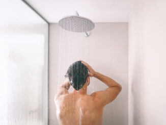 Man taking a shower washing hair with shampoo product under water falling from luxury rain shower head