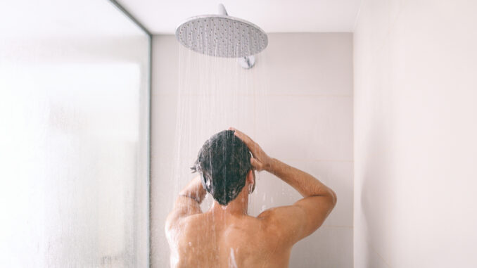 Man taking a shower washing hair with shampoo product under water falling from luxury rain shower head