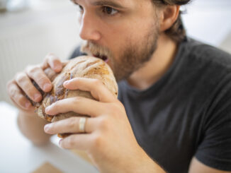 Surprised-looking man at white table calmly eating bread.