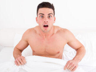 Surprised and shocked half naked young man in bed looking down at his underwear at his penis