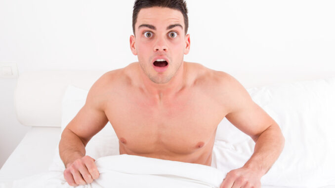 Surprised and shocked half naked young man in bed looking down at his underwear at his penis